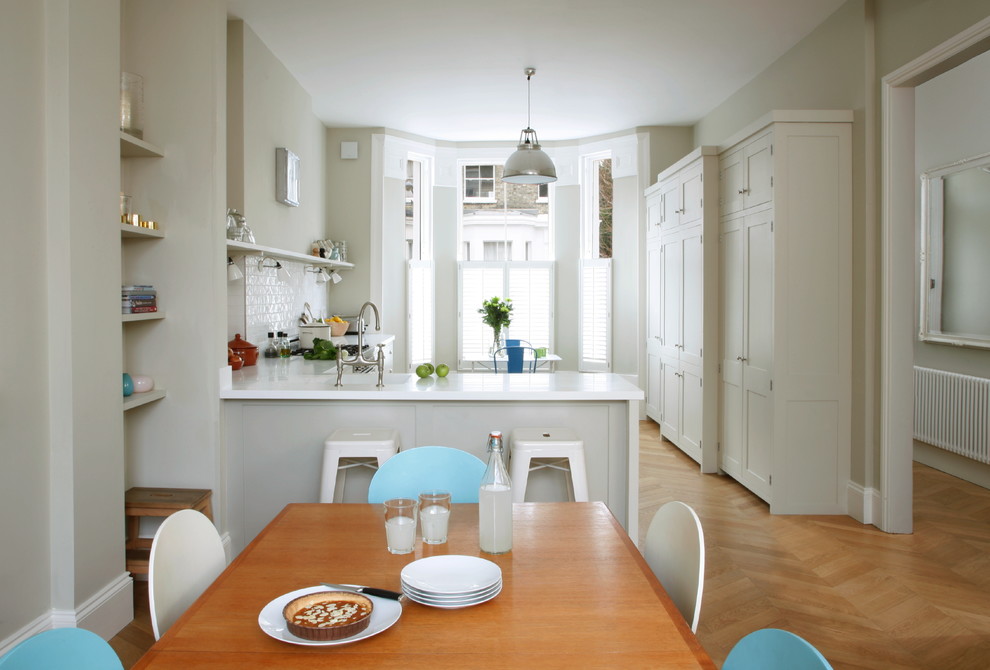 Photo of a medium sized classic l-shaped kitchen/diner in London with a submerged sink, shaker cabinets, white cabinets, composite countertops, white splashback, metro tiled splashback, stainless steel appliances, light hardwood flooring and no island.