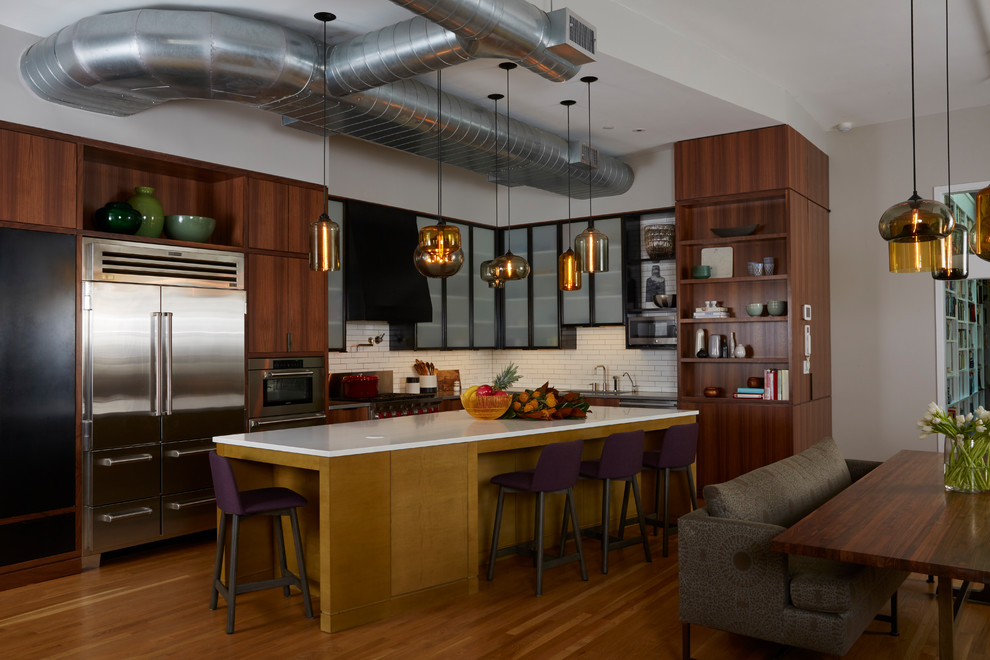 This is an example of an industrial l-shaped eat-in kitchen in New York with medium wood cabinets, white splashback, subway tile splashback, stainless steel appliances, medium hardwood floors and with island.