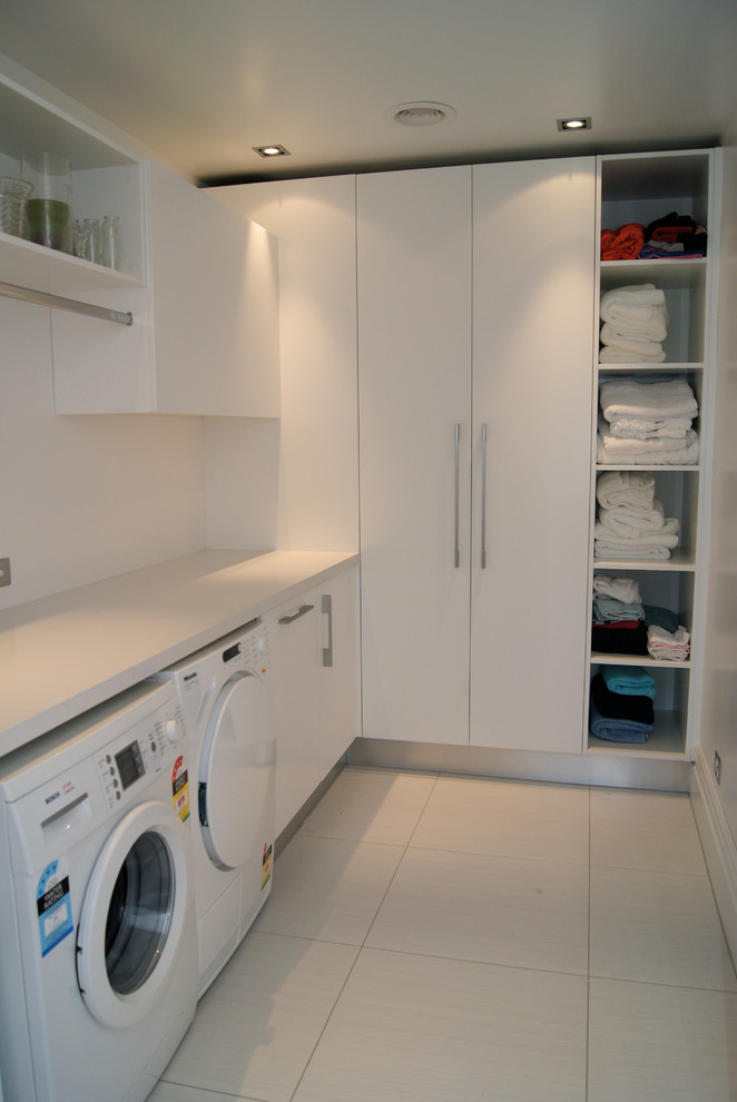 This is an example of a small contemporary l-shaped dedicated laundry room in Auckland with white cabinets, quartz benchtops, an undermount sink, flat-panel cabinets, white walls, ceramic floors and a side-by-side washer and dryer.