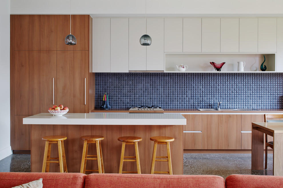 Photo of a large contemporary galley open plan kitchen in Melbourne with a drop-in sink, flat-panel cabinets, medium wood cabinets, blue splashback, with island, granite benchtops, ceramic splashback, stainless steel appliances, concrete floors and grey floor.