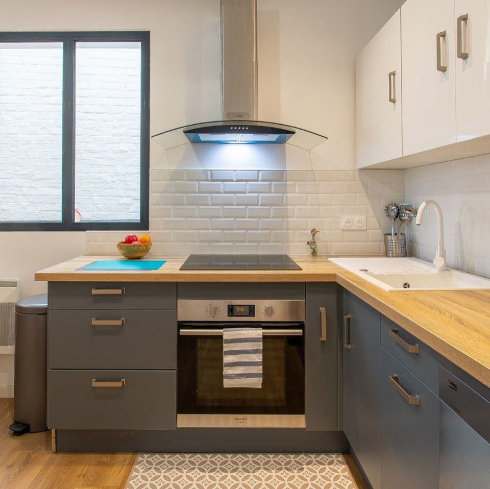Small scandinavian l-shaped open plan kitchen in Lille with a single-bowl sink, grey cabinets, wood benchtops, white splashback, subway tile splashback, stainless steel appliances, light hardwood floors and no island.