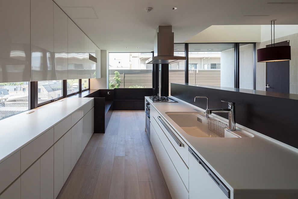 Photo of an expansive modern galley open plan kitchen in Tokyo with an integrated sink, flat-panel cabinets, white cabinets, solid surface benchtops, white splashback, glass sheet splashback, stainless steel appliances, plywood floors and beige floor.
