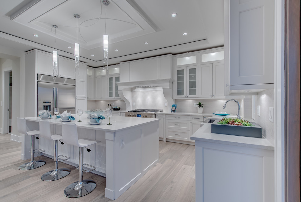 Mid-sized transitional u-shaped light wood floor and beige floor open concept kitchen photo in Vancouver with white cabinets, recessed-panel cabinets, white backsplash, stainless steel appliances, an island and a farmhouse sink