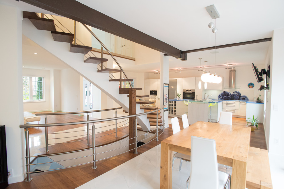 This is an example of a large modern wood curved staircase in Toronto with open risers and metal railing.
