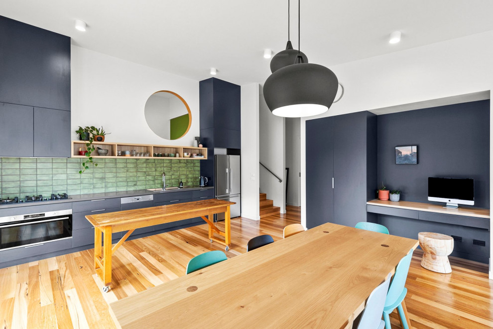 This is an example of a mid-sized single-wall open plan kitchen in Melbourne with a drop-in sink, flat-panel cabinets, grey cabinets, solid surface benchtops, green splashback, ceramic splashback, stainless steel appliances, medium hardwood floors, with island and grey benchtop.
