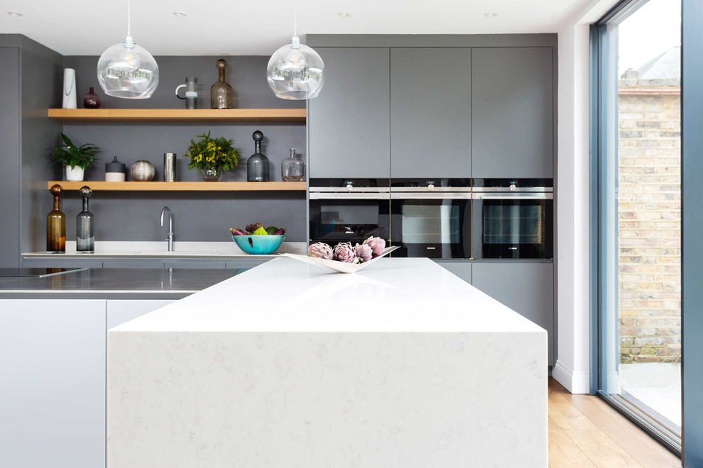 Contemporary single-wall kitchen in London with flat-panel cabinets, light hardwood floors and with island.