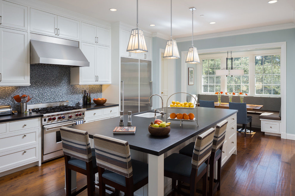This is an example of an expansive transitional eat-in kitchen in San Francisco with an undermount sink, shaker cabinets, white cabinets, soapstone benchtops, blue splashback, glass sheet splashback, stainless steel appliances, medium hardwood floors, with island and brown floor.