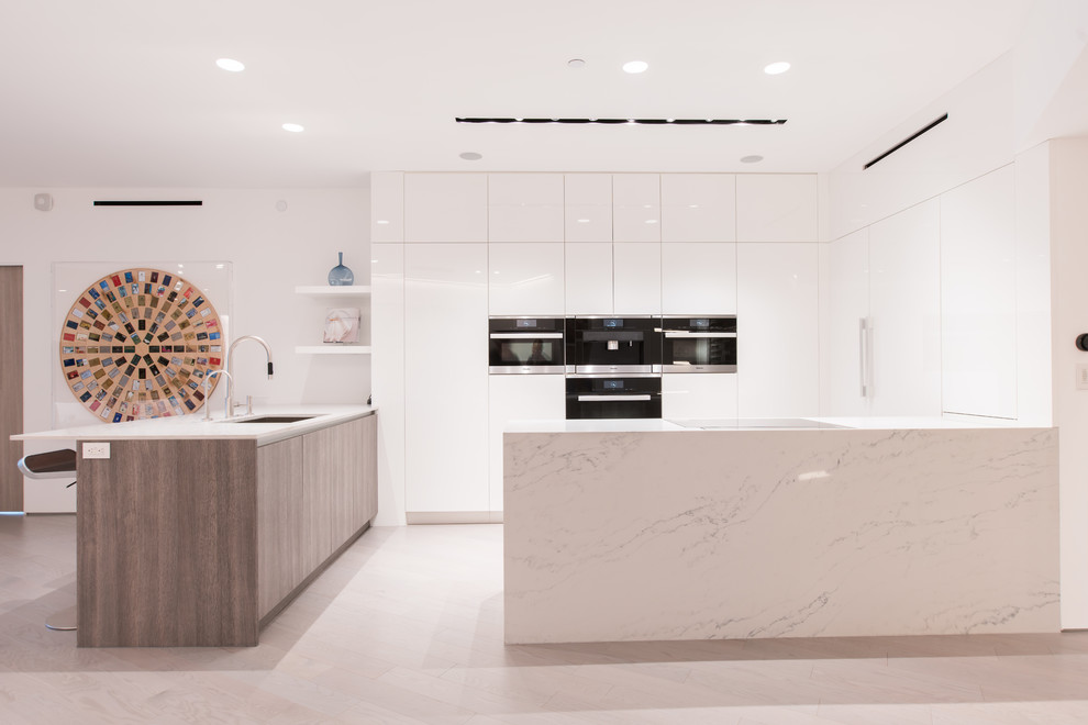 This is an example of a contemporary u-shaped open plan kitchen in Los Angeles with an undermount sink, flat-panel cabinets, white cabinets, panelled appliances, a peninsula, beige floor and white benchtop.