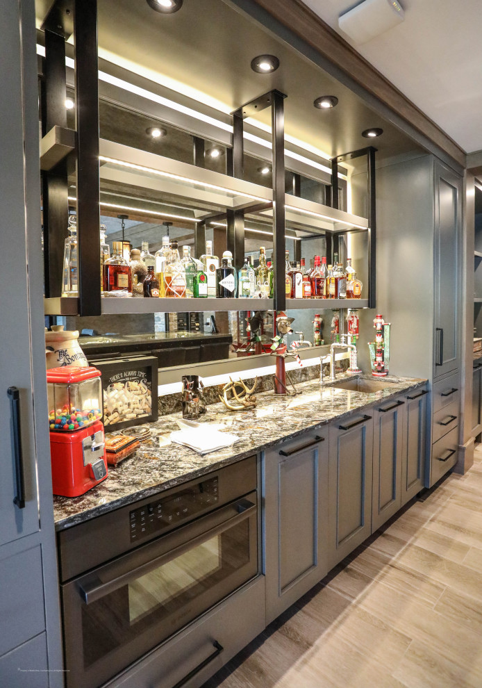 Photo of a large traditional l-shaped seated home bar in Other with an undermount sink, beaded inset cabinets, grey cabinets, glass benchtops, glass sheet splashback and porcelain floors.