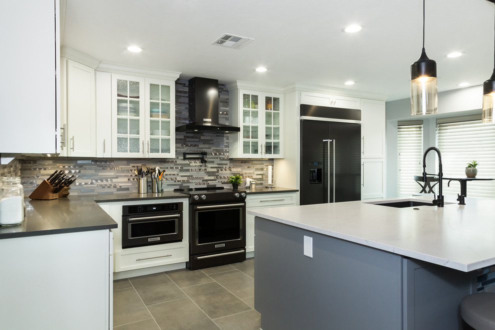 Open concept kitchen - mid-sized transitional l-shaped porcelain tile and gray floor open concept kitchen idea in Phoenix with an undermount sink, shaker cabinets, white cabinets, quartz countertops, gray backsplash, glass tile backsplash, black appliances, an island and gray countertops