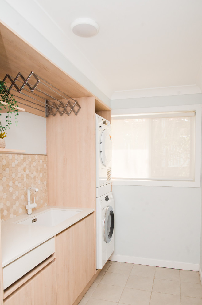 Small scandinavian single-wall dedicated laundry room in Brisbane with an undermount sink, flat-panel cabinets, light wood cabinets, quartz benchtops, porcelain floors, a stacked washer and dryer, brown floor and white benchtop.