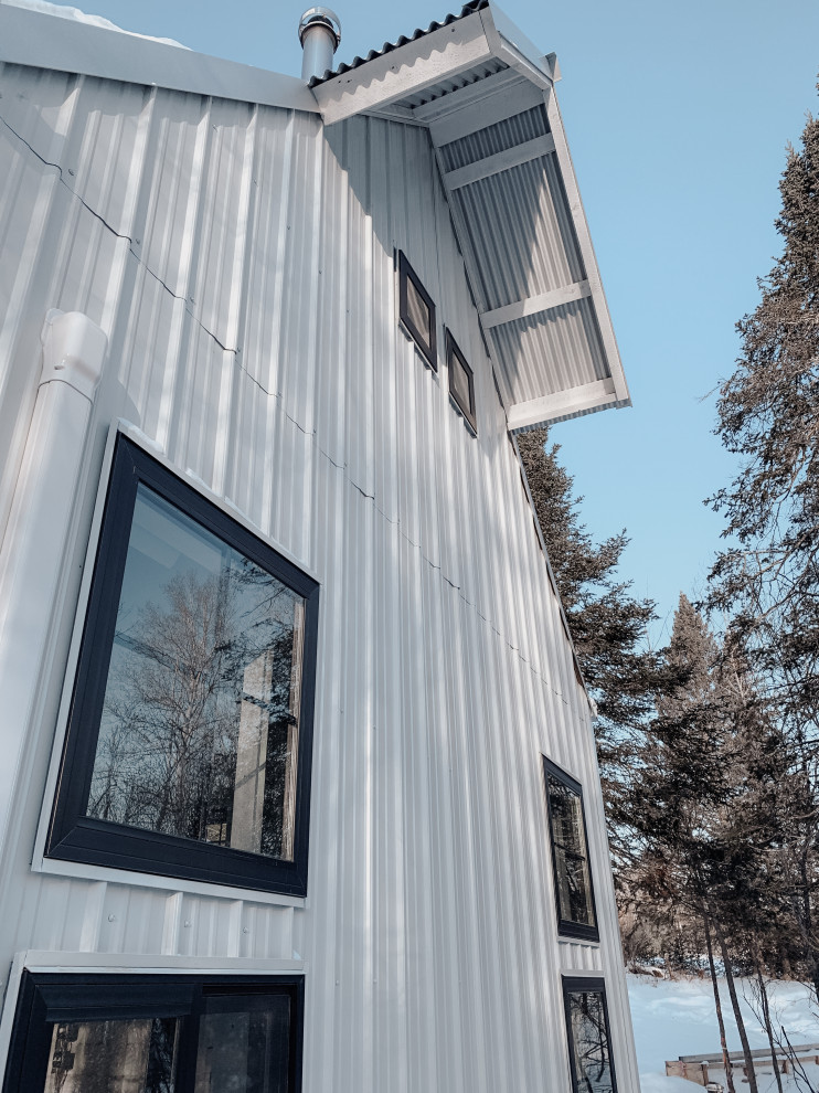 Imagen de fachada de casa blanca de estilo de casa de campo pequeña de dos plantas con revestimiento de metal, tejado a dos aguas, tejado de metal y panel y listón