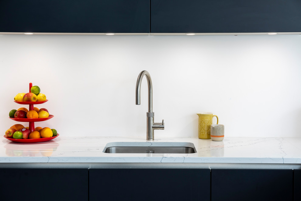 Inspiration for a contemporary kitchen in London with a single-bowl sink, solid surface benchtops and black appliances.