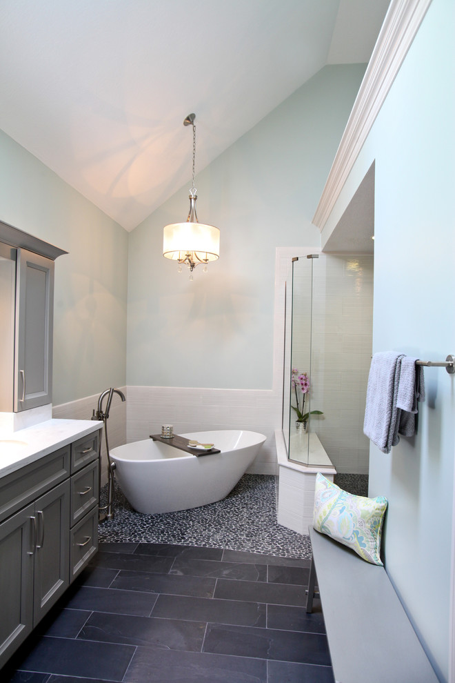 Transitional bathroom in Indianapolis with recessed-panel cabinets, grey cabinets, a freestanding tub, a corner shower, white tile, blue walls and pebble tile floors.