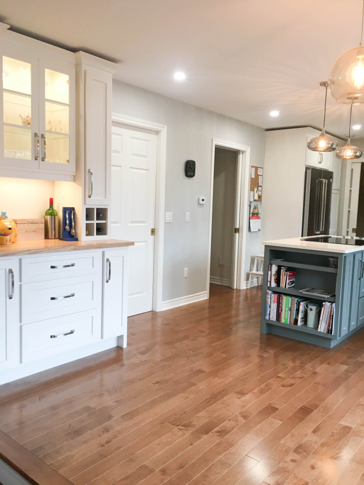 Example of a mid-sized transitional l-shaped medium tone wood floor and brown floor enclosed kitchen design with a double-bowl sink, shaker cabinets, gray cabinets, quartz countertops, white backsplash, porcelain backsplash, stainless steel appliances, an island and white countertops