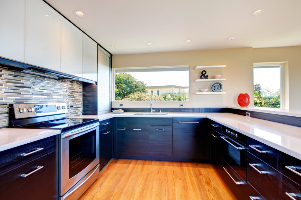 Photo of a mid-sized contemporary u-shaped open plan kitchen in Other with an undermount sink, flat-panel cabinets, black cabinets, quartz benchtops, multi-coloured splashback, matchstick tile splashback, stainless steel appliances, medium hardwood floors, a peninsula, beige floor and white benchtop.