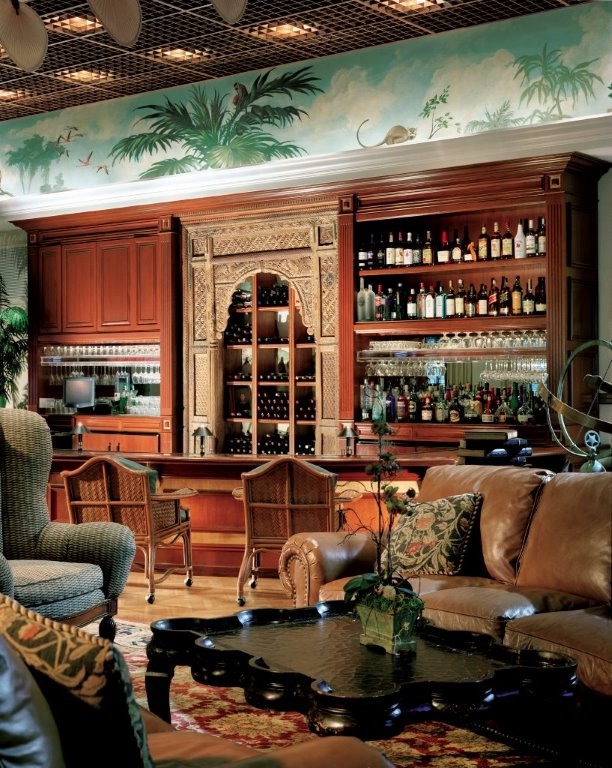 This is an example of a large tropical single-wall seated home bar in Las Vegas with open cabinets, medium wood cabinets, wood benchtops, mirror splashback, light hardwood floors and beige floor.