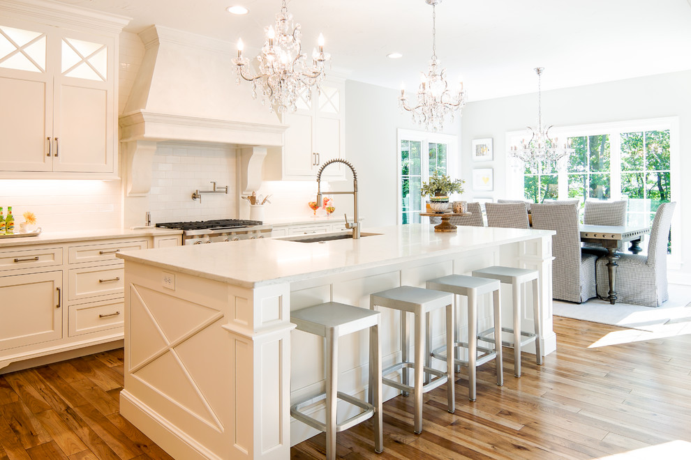 This is an example of a traditional eat-in kitchen in Cleveland with white cabinets, stainless steel appliances, with island, an undermount sink, shaker cabinets, white splashback, subway tile splashback, medium hardwood floors and white benchtop.