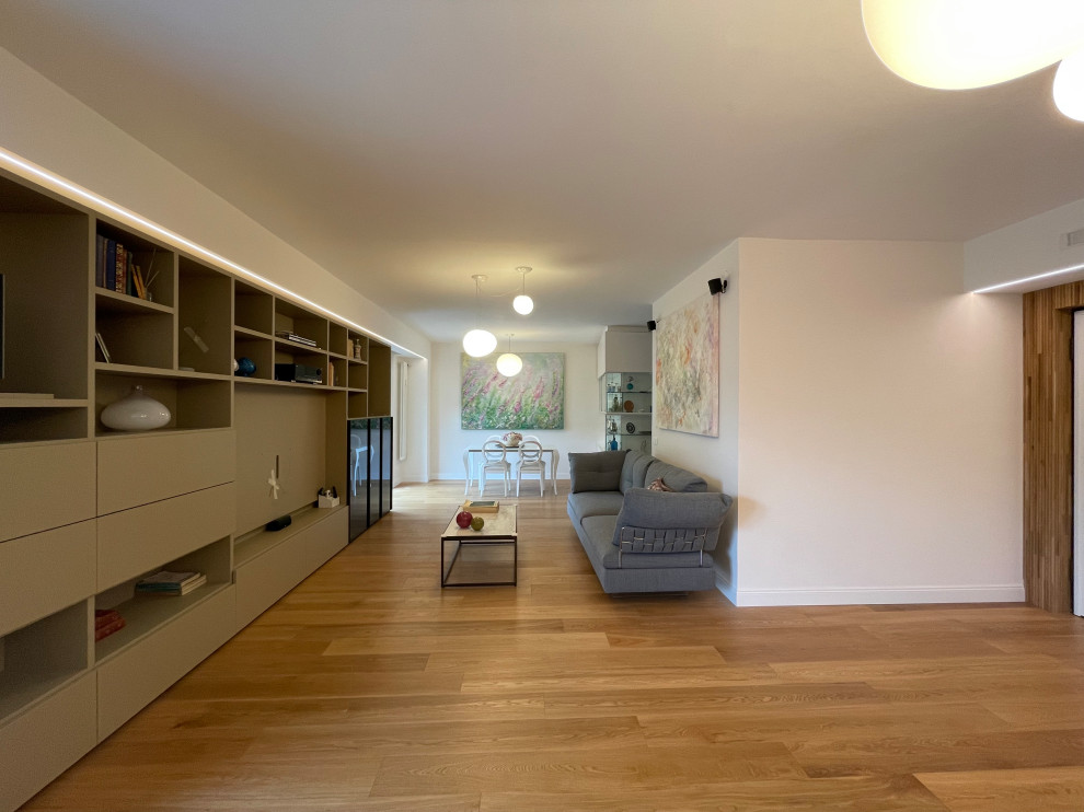 This is an example of a large contemporary open concept living room in Rome with a library, white walls, dark hardwood floors, a hanging fireplace, a built-in media wall and brown floor.