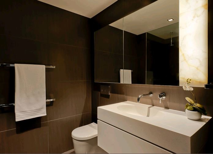 This is an example of a small contemporary bathroom in Melbourne with recessed-panel cabinets, white cabinets, a wall-mount toilet, brown tile, an integrated sink, white benchtops, a single vanity and a floating vanity.