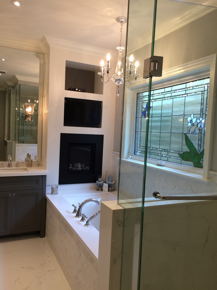 Photo of a mid-sized traditional master bathroom in Toronto with an undermount sink, recessed-panel cabinets, grey cabinets, solid surface benchtops, a drop-in tub, a corner shower, a one-piece toilet, white tile, stone tile, grey walls and porcelain floors.