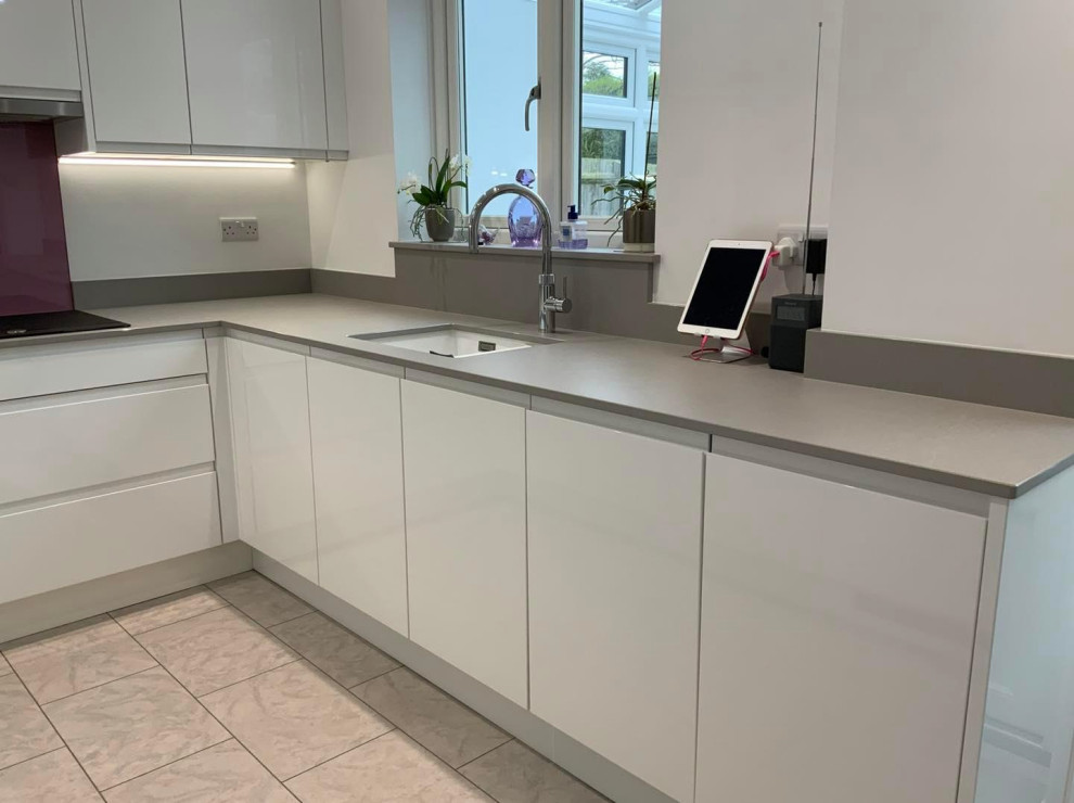 Design ideas for a mid-sized contemporary u-shaped kitchen with flat-panel cabinets, white cabinets, quartzite benchtops, pink splashback, glass sheet splashback, panelled appliances, no island and grey benchtop.