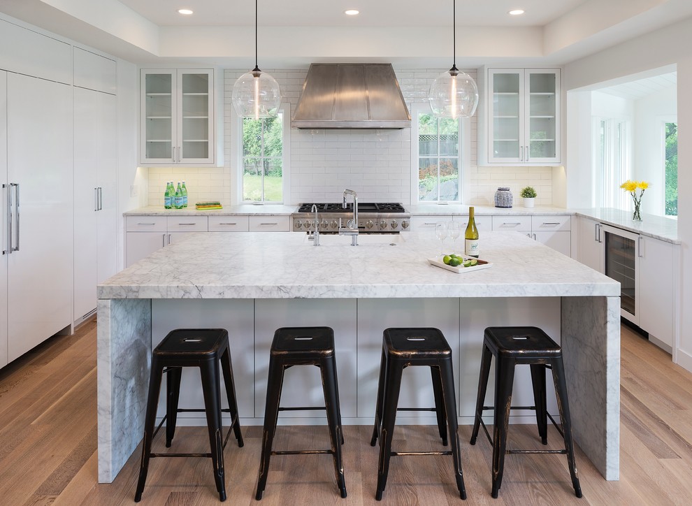 This is an example of a contemporary u-shaped kitchen in Minneapolis with white cabinets, white splashback, subway tile splashback, stainless steel appliances, medium hardwood floors, with island and flat-panel cabinets.