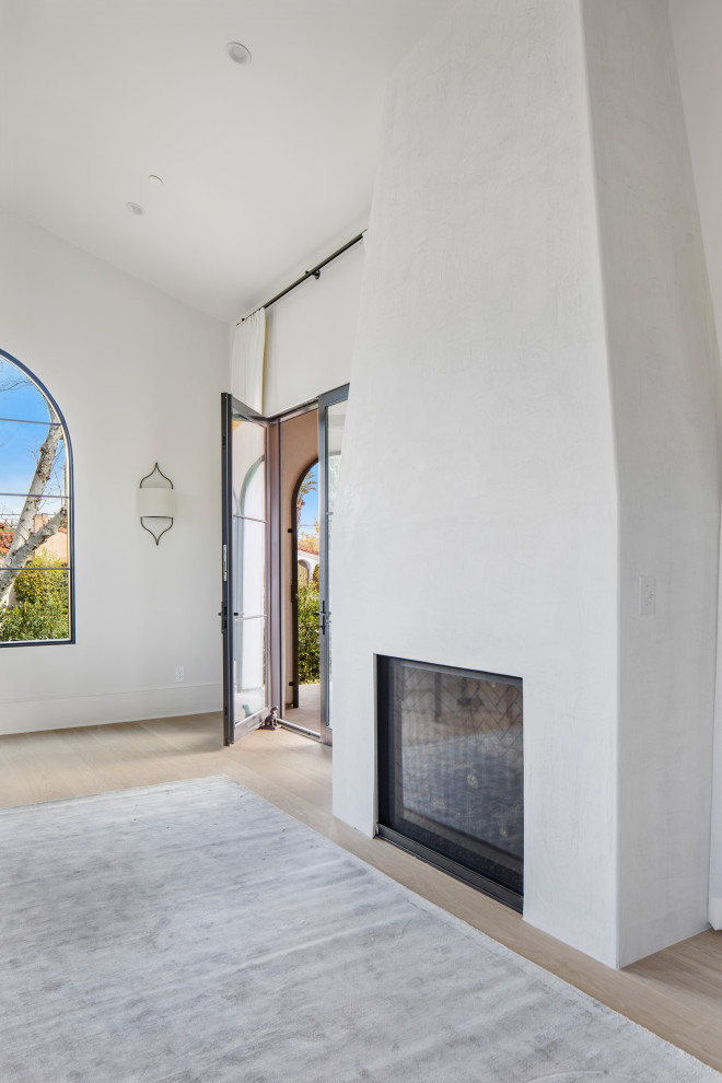 Large mediterranean formal enclosed living room in Los Angeles with white walls, light hardwood flooring, a standard fireplace, a plastered fireplace surround, a wall mounted tv, beige floors and a vaulted ceiling.