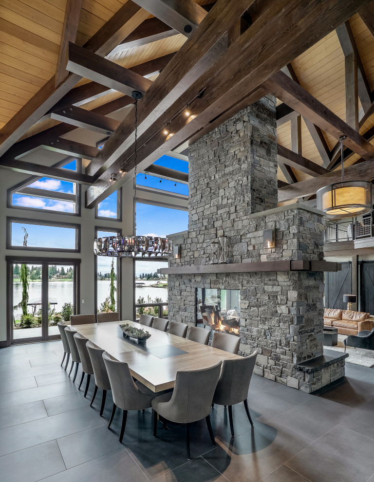 This is an example of a country open plan dining in Seattle with grey walls, a two-sided fireplace, a stone fireplace surround and grey floor.