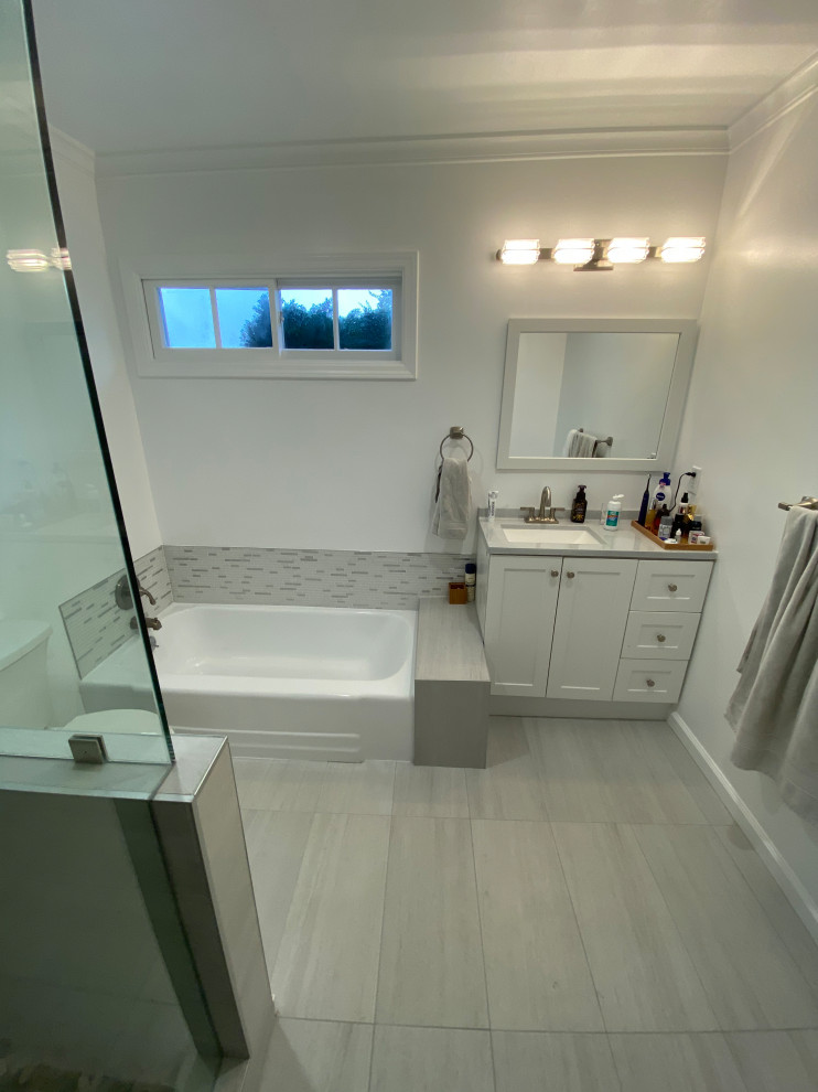 Cette image montre une salle de bain principale minimaliste de taille moyenne avec un placard à porte shaker, des portes de placard blanches, une baignoire en alcôve, une douche ouverte, WC à poser, un carrelage gris, des carreaux de porcelaine, un mur blanc, un sol en carrelage de porcelaine, un plan de toilette en quartz, un sol gris, un plan de toilette blanc, meuble simple vasque et meuble-lavabo sur pied.