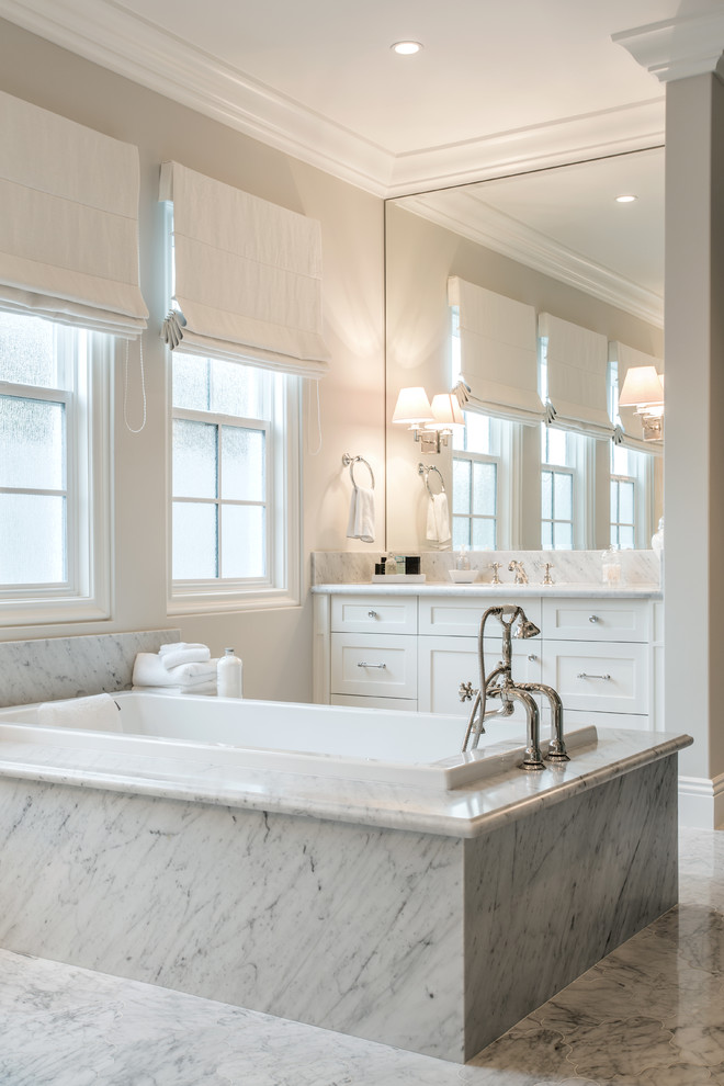 Photo of a large transitional master bathroom in Orange County with shaker cabinets, white cabinets, a drop-in tub, an undermount sink, marble benchtops, white tile, stone tile, beige walls, marble floors and white benchtops.