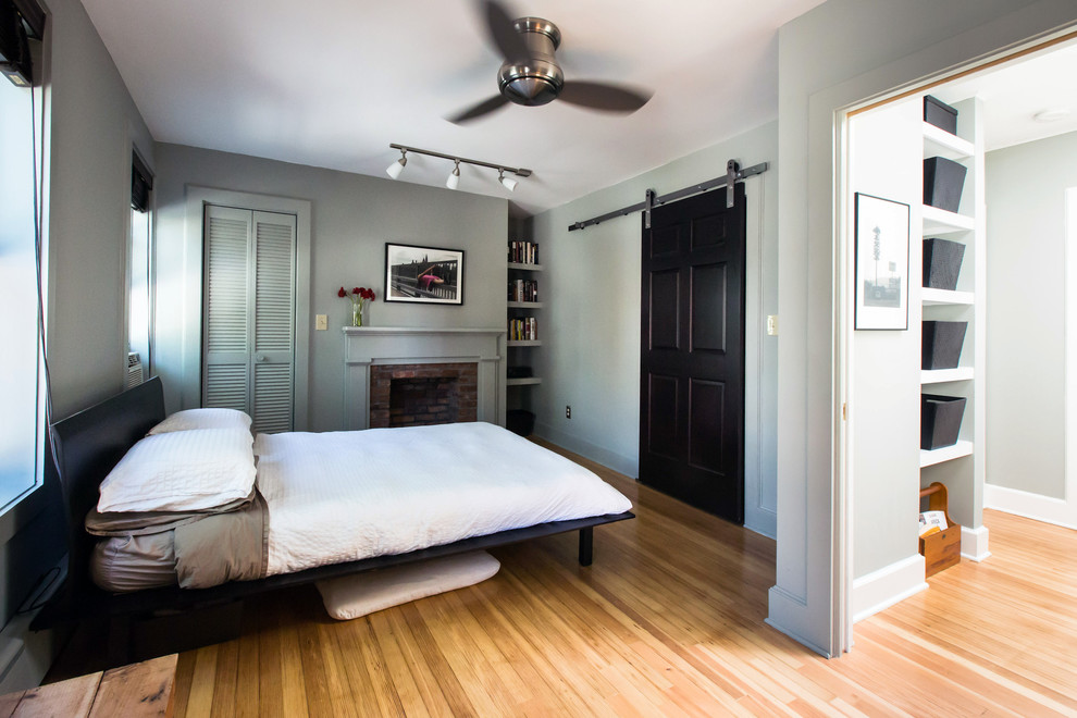 This is an example of a transitional bedroom in Boston with grey walls, medium hardwood floors, a standard fireplace and a brick fireplace surround.