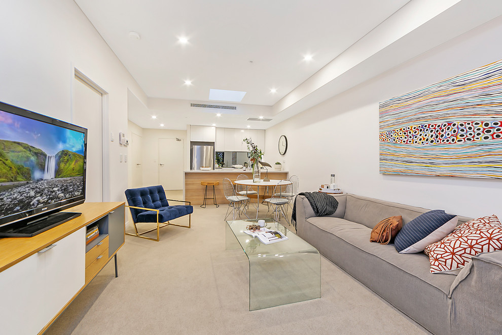 This is an example of a modern open concept living room in Sydney with white walls, carpet, a freestanding tv and beige floor.