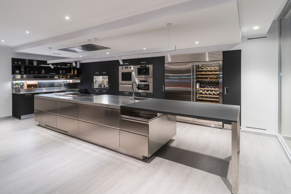 Inspiration for an industrial l-shaped kitchen in Other with an integrated sink, flat-panel cabinets, black cabinets, stainless steel benchtops, stainless steel appliances, with island and black benchtop.