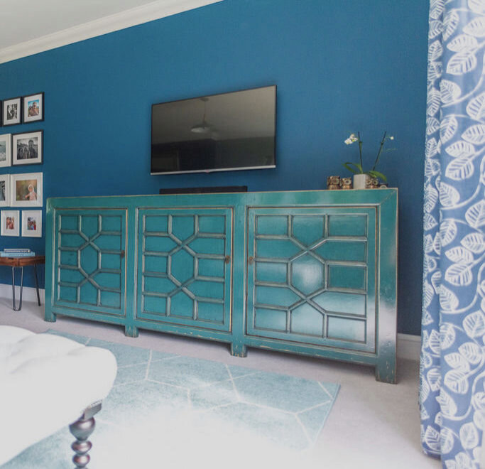 Стильный дизайн: изолированная гостиная комната среднего размера в стиле рустика с синими стенами, ковровым покрытием, стандартным камином, фасадом камина из камня, телевизором на стене, бежевым полом, балками на потолке и кирпичными стенами - последний тренд