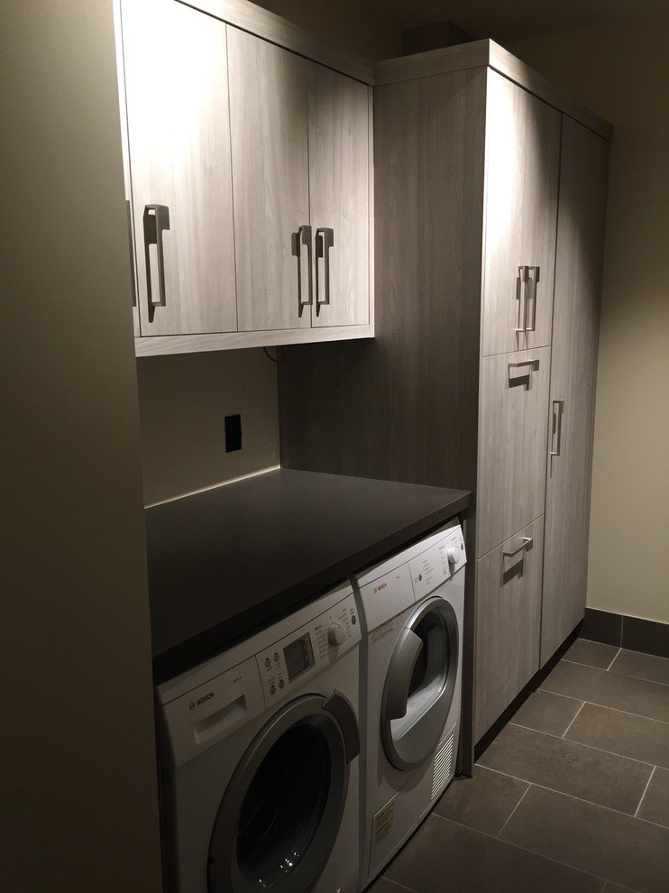 Design ideas for a mid-sized modern galley dedicated laundry room in Calgary with flat-panel cabinets, grey cabinets, laminate benchtops, beige walls, ceramic floors and a side-by-side washer and dryer.
