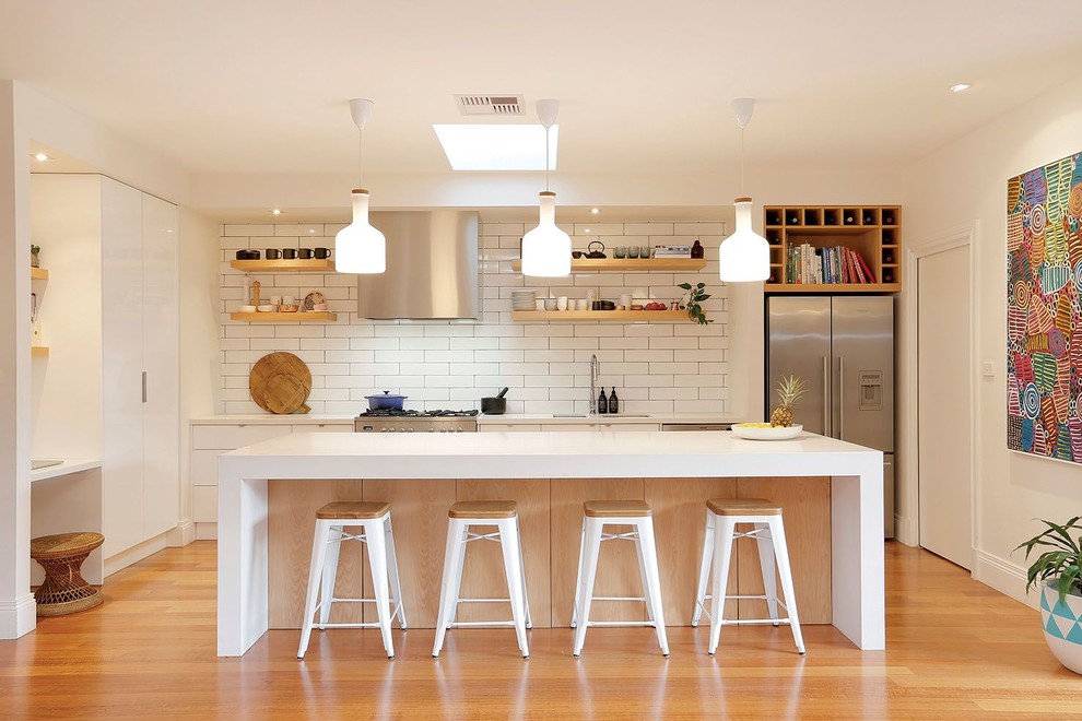 Photo of a mid-sized scandinavian galley kitchen in Melbourne with an undermount sink, flat-panel cabinets, white cabinets, white splashback, stainless steel appliances, with island, subway tile splashback and medium hardwood floors.