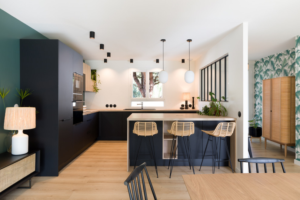 This is an example of a large contemporary l-shaped kitchen in Bordeaux with an integrated sink, beaded inset cabinets, black cabinets, wood benchtops, green splashback, light hardwood floors, with island, beige floor, beige benchtop and wood.
