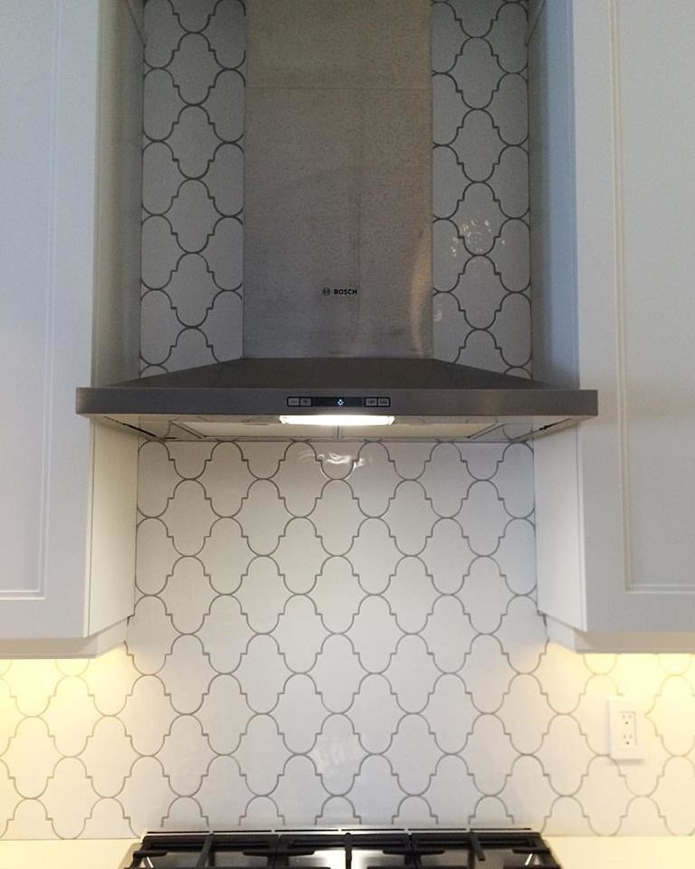 Inspiration for a modern home design remodel in Vancouver with a farmhouse sink, raised-panel cabinets, white cabinets, quartzite countertops, white backsplash, mosaic tile backsplash, stainless steel appliances and an island