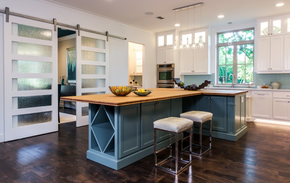 Photo of a traditional kitchen in Dallas with an undermount sink, shaker cabinets, white cabinets, blue splashback, glass tile splashback, stainless steel appliances, dark hardwood floors, wood benchtops and with island.