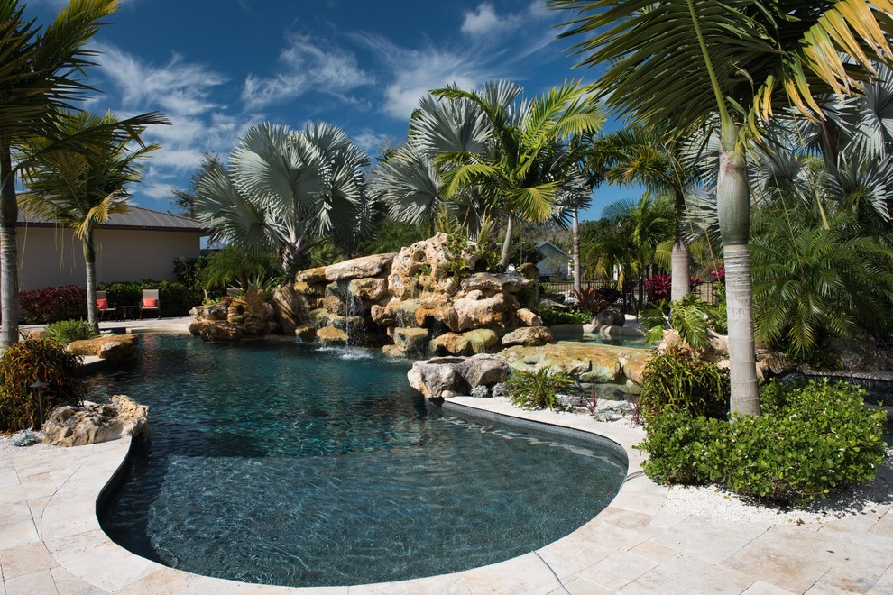 This is an example of a mid-sized tropical backyard custom-shaped pool in New York with a water feature and natural stone pavers.
