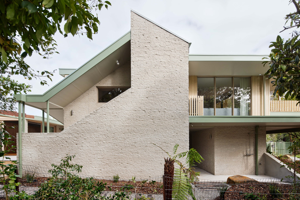 Réalisation d'une façade de maison beige marine en brique et planches et couvre-joints à un étage et de taille moyenne avec un toit à deux pans et un toit en métal.