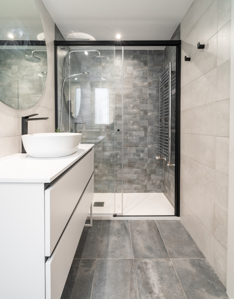 Пример оригинального дизайна: серо-белая ванная комната среднего размера в скандинавском стиле с плоскими фасадами, белыми фасадами, душевой комнатой, унитазом-моноблоком, серой плиткой, керамической плиткой, серыми стенами, полом из керамической плитки, душевой кабиной, раковиной с несколькими смесителями, столешницей из искусственного камня, серым полом, душем с раздвижными дверями, белой столешницей, тумбой под одну раковину и подвесной тумбой
