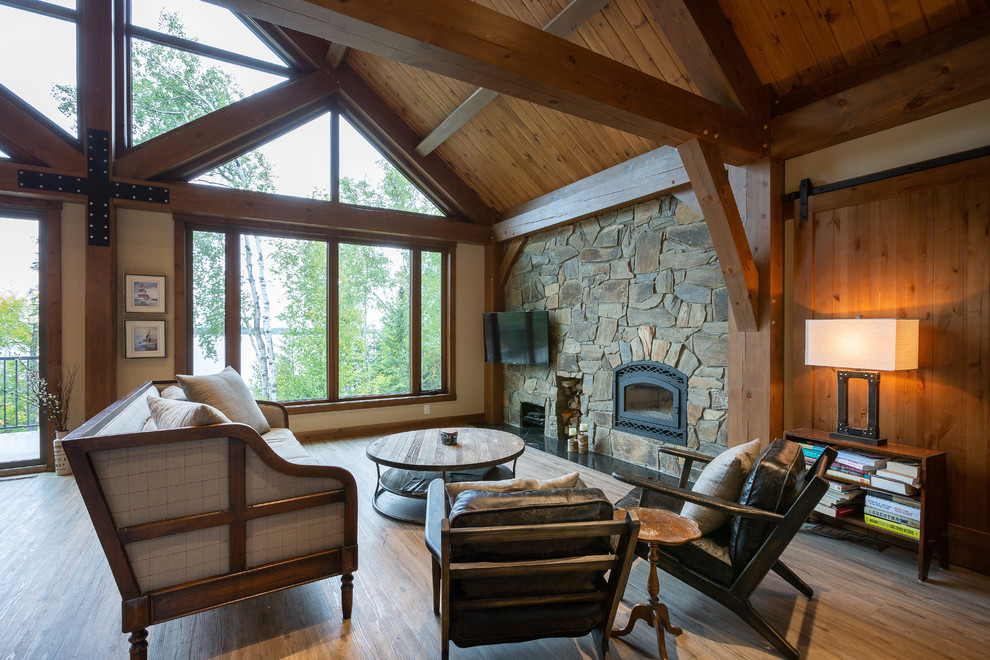 This is an example of a large country open concept family room in Other with beige walls, linoleum floors, a wood stove, a stone fireplace surround, a wall-mounted tv and brown floor.