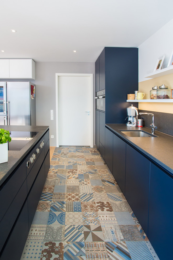 Mid-sized contemporary galley eat-in kitchen in Stuttgart with a single-bowl sink, granite benchtops, grey splashback, stone slab splashback, black appliances, porcelain floors, with island, blue cabinets and flat-panel cabinets.