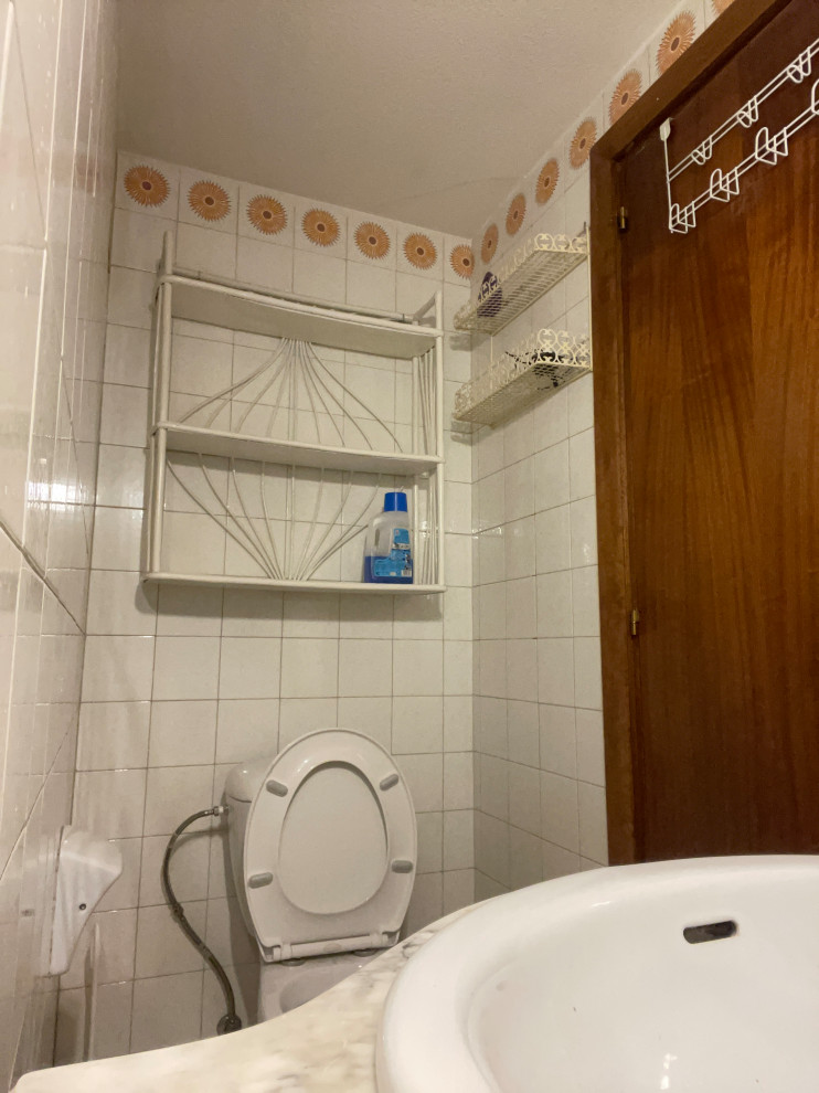 This is an example of a medium sized retro cloakroom in Madrid with freestanding cabinets, beige cabinets, a one-piece toilet, white tiles, ceramic tiles, white walls, ceramic flooring, a trough sink, engineered stone worktops, beige floors, white worktops, a freestanding vanity unit, a drop ceiling and brick walls.