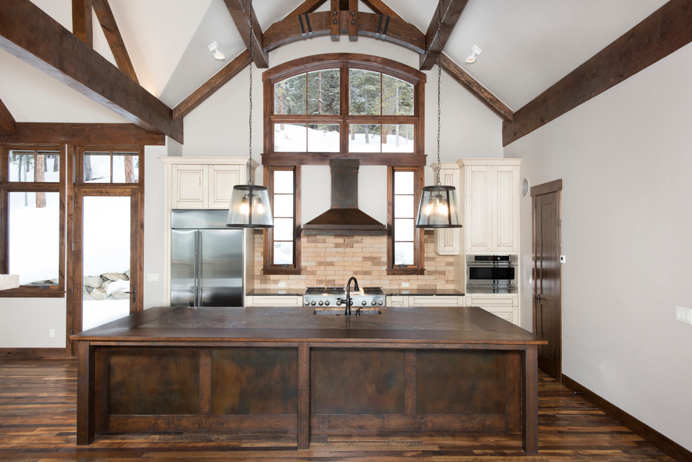Photo of a country l-shaped open plan kitchen in Denver with an undermount sink, beaded inset cabinets, white cabinets, beige splashback, stainless steel appliances, medium hardwood floors, with island and brown floor.
