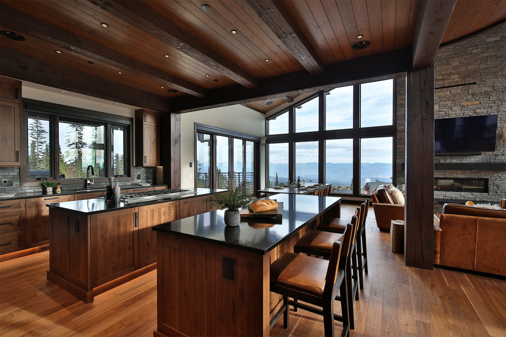 Open concept kitchen - large rustic u-shaped medium tone wood floor, brown floor and exposed beam open concept kitchen idea with an undermount sink, shaker cabinets, medium tone wood cabinets, quartz countertops, gray backsplash, slate backsplash, stainless steel appliances, two islands and black countertops