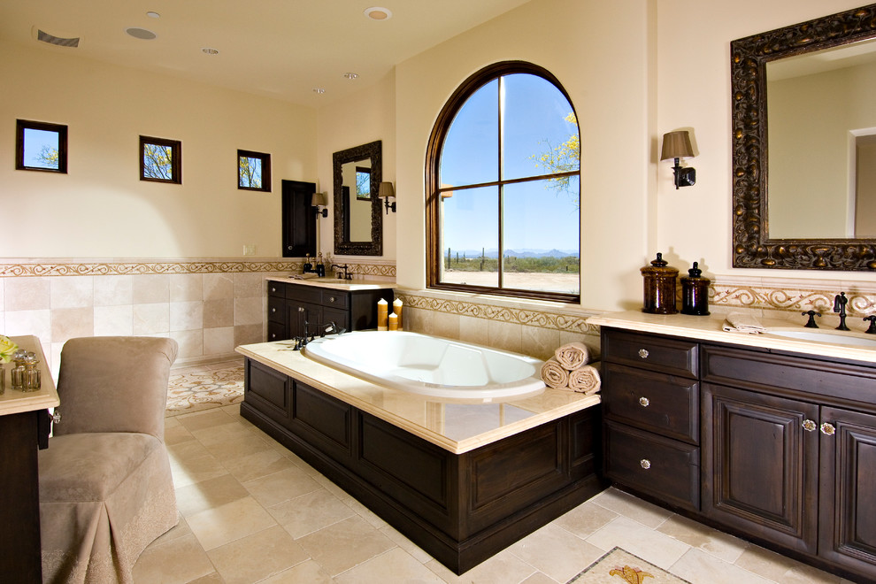 Design ideas for a mediterranean bathroom in Phoenix with an undermount sink, raised-panel cabinets, dark wood cabinets, a drop-in tub and beige tile.