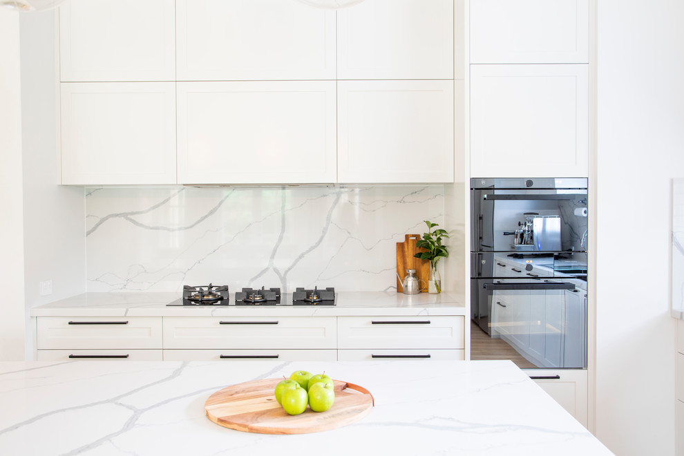 Expansive transitional l-shaped open plan kitchen in Sydney with a double-bowl sink, shaker cabinets, white cabinets, quartz benchtops, white splashback, marble splashback, stainless steel appliances, light hardwood floors, with island, beige floor and white benchtop.